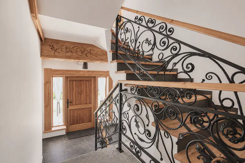 Wejście do domu z drewnianymi schodami i ręcznie kutą metalową balustradą